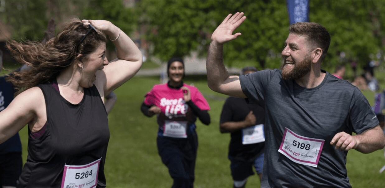 Race for Life participants running and smiling while giving each other a high five.