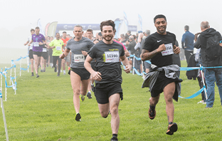 Men running on a grassy route, with the start line in the background.