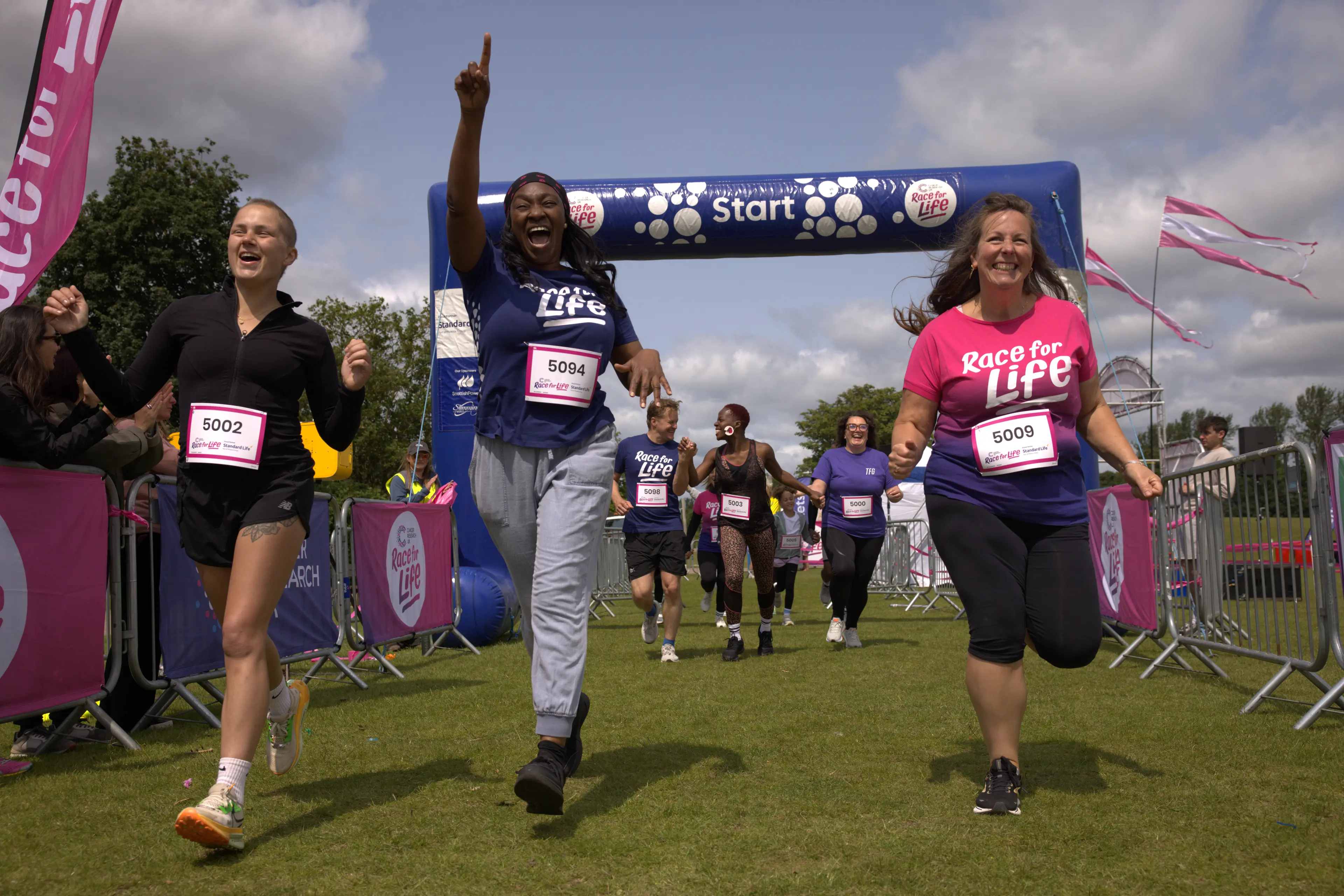 Three race for life runners crossing the finish line and smiling.