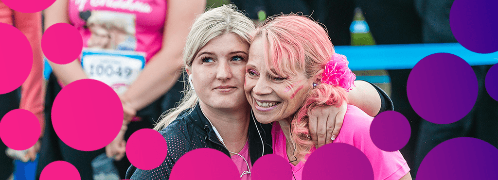 Two women in Race for Life t-shirts embracing with white headphones in their ears.