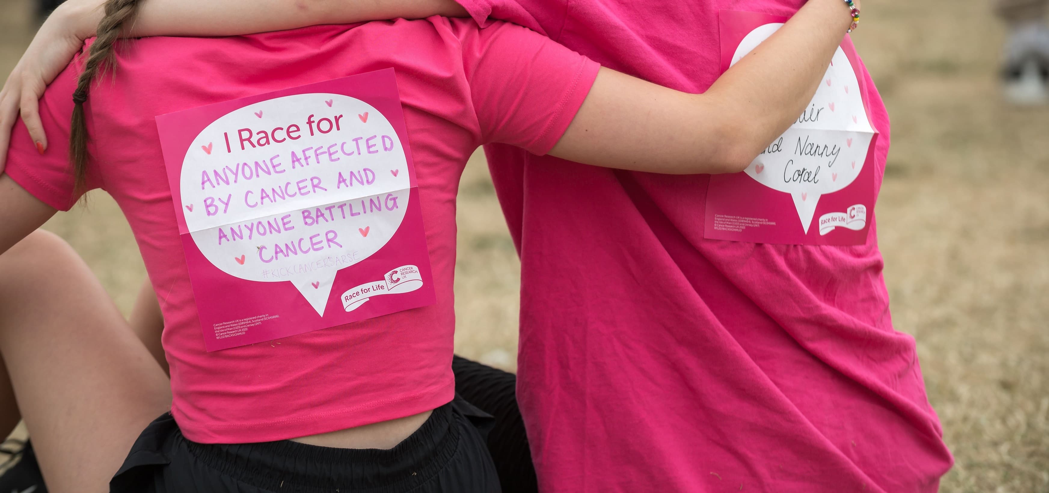 Two people hugging. The back sign reads 'I race for anyone affected by cancer and anyone battling cancer'.
